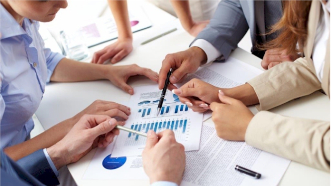 Attēls: cilvēki ap galdu apspriež grafikus