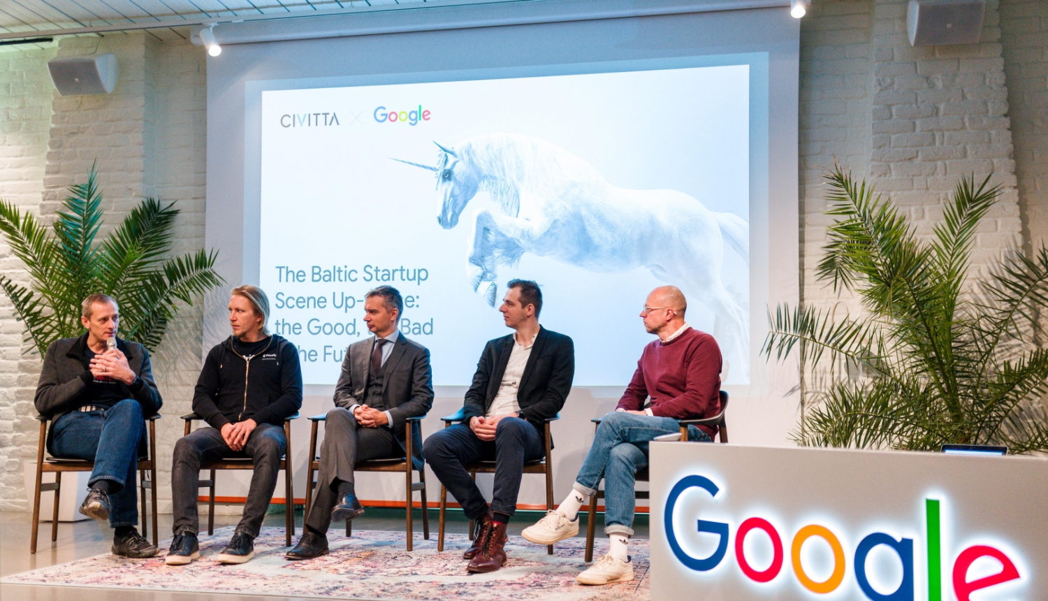 vīrieši sēž uz krēsliem uz skatuves un sarunājas. priekšpusē Google logo.