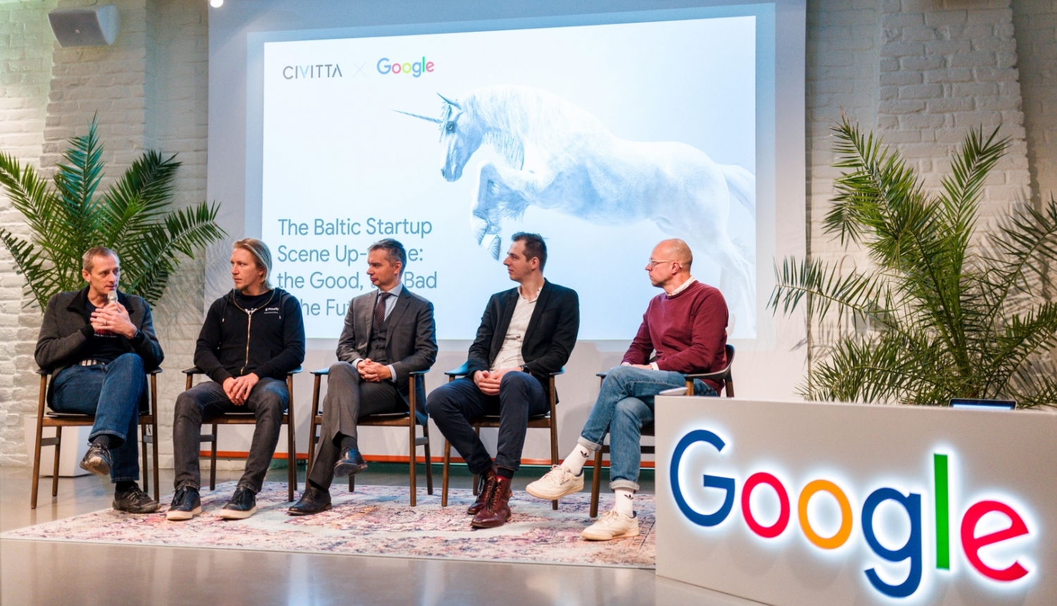 vīrieši sēž uz krēsliem uz skatuves un sarunājas. priekšpusē Google logo.